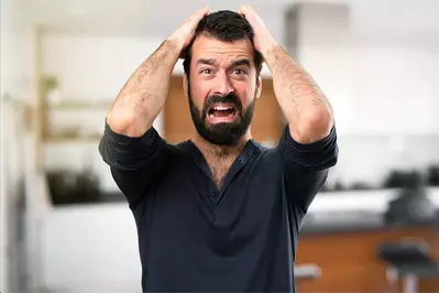 man with hands on his head screaming in distress
