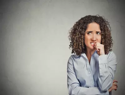 Woman biting her thumb nail and making a worried face while looking upwards