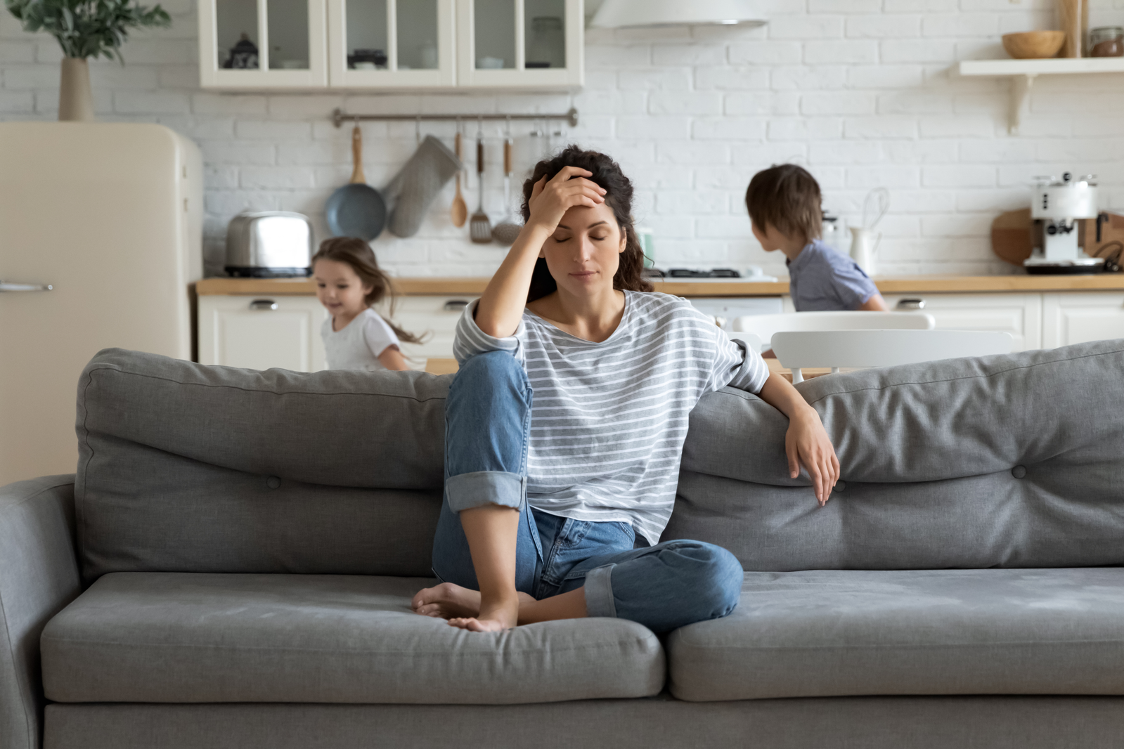 woman holding her head with kids running in the background